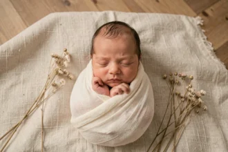 Nouveau-né endormi enveloppé dans un lange ivoire lors d'un photoshoot naissance en studio minimaliste